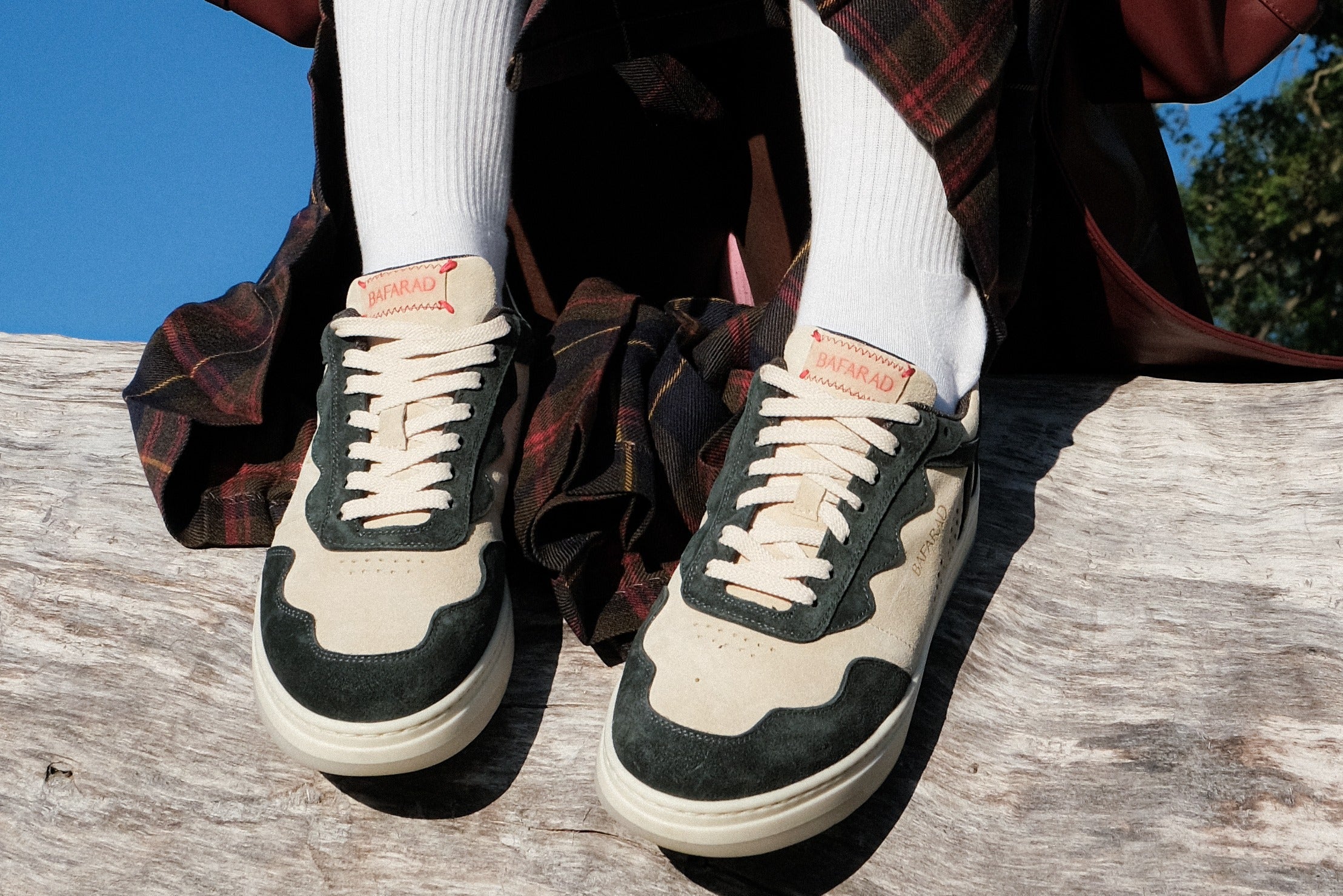 Person wearing white socks and black and beige sneakers sitting on a wooden surface with a plaid garment.